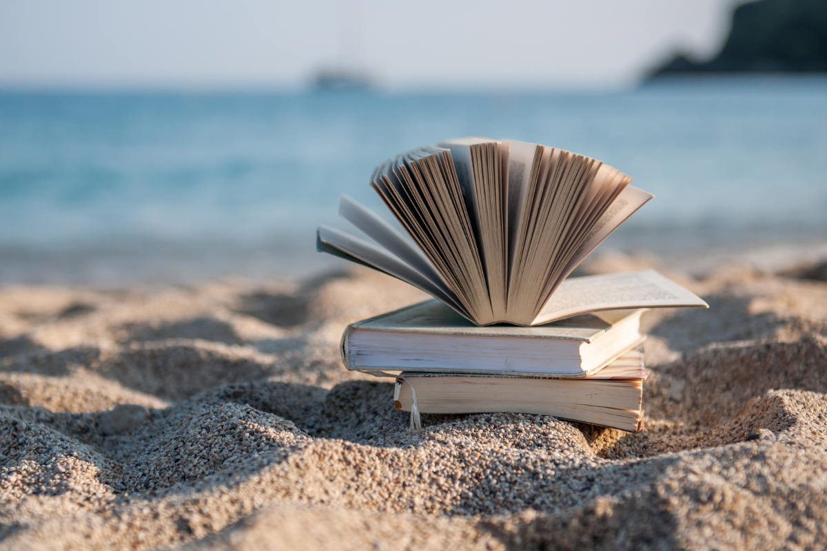 Collection de livres posée sur une serviette de plage avec une vue sur l'océan
