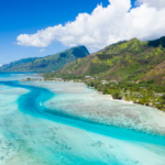 Plage de sable blanc en Polynésie avec une mer turquoise et des montagnes en arrière-plan
