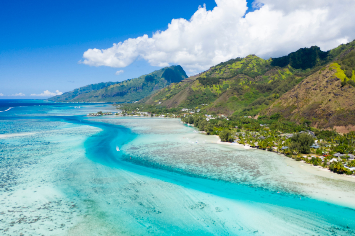 Plage de sable blanc en Polynésie avec une mer turquoise et des montagnes en arrière-plan
